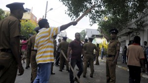 People hold wooden poles as they stand next to police officers in Colombo